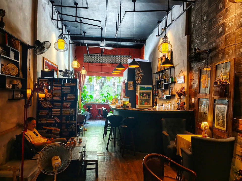 本、植物、ペンダントライト、緑のバーカウンターがある温かい Whisfee Café 店内